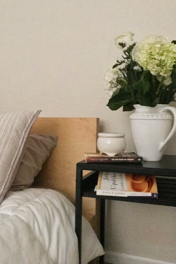 White flowers on a black nightstand and wood Ikea Malm bed.