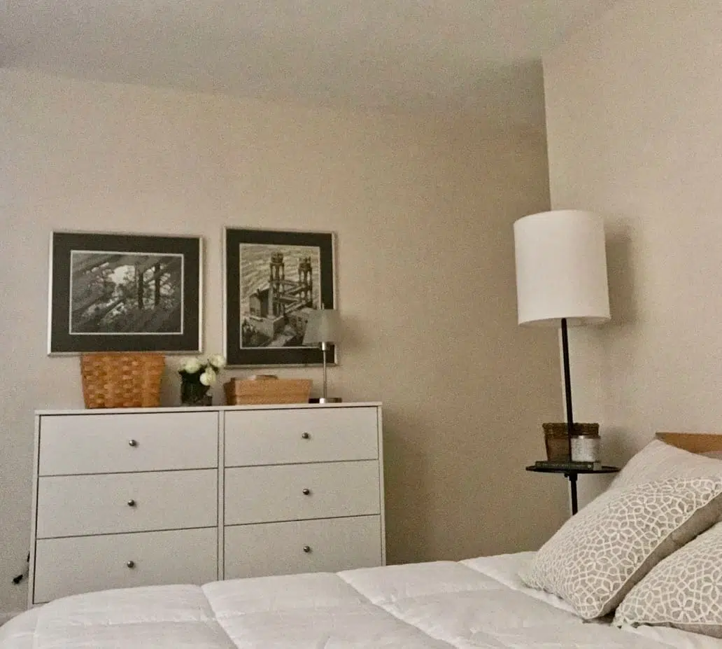 White dresser and bed with Escher prints and green beige pillows.