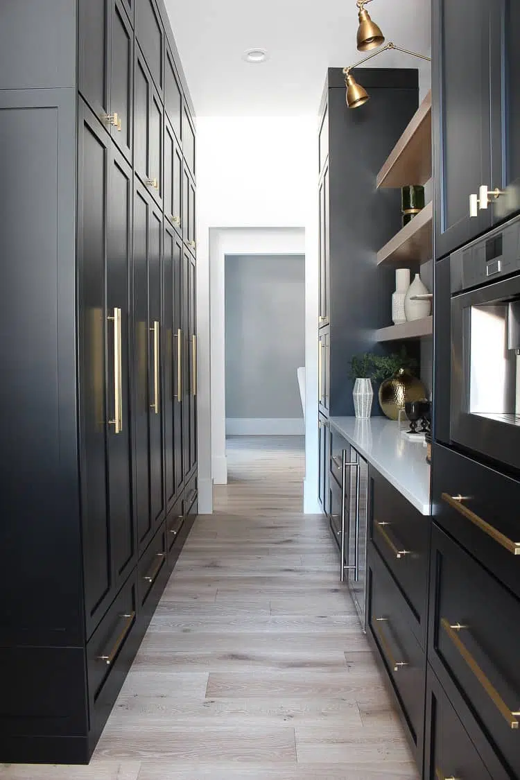 Butler's pantry with black cabinets, gold hardware and lights and white counters.