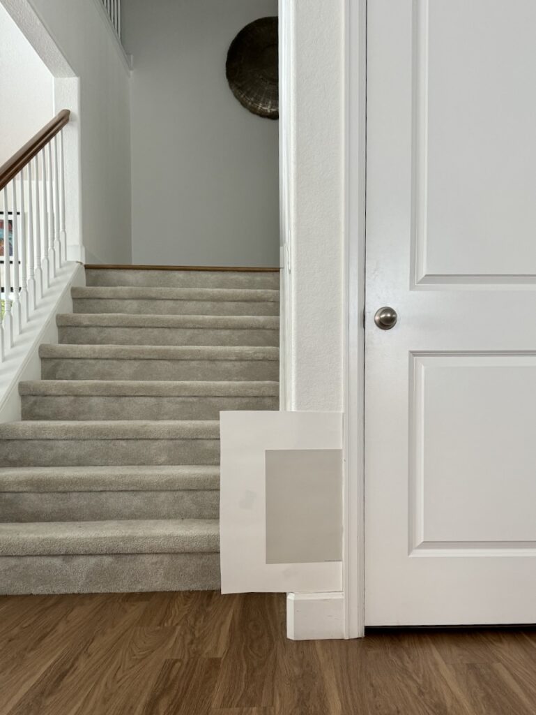 A gray color swatch is tested next to white trim and beige carpet.