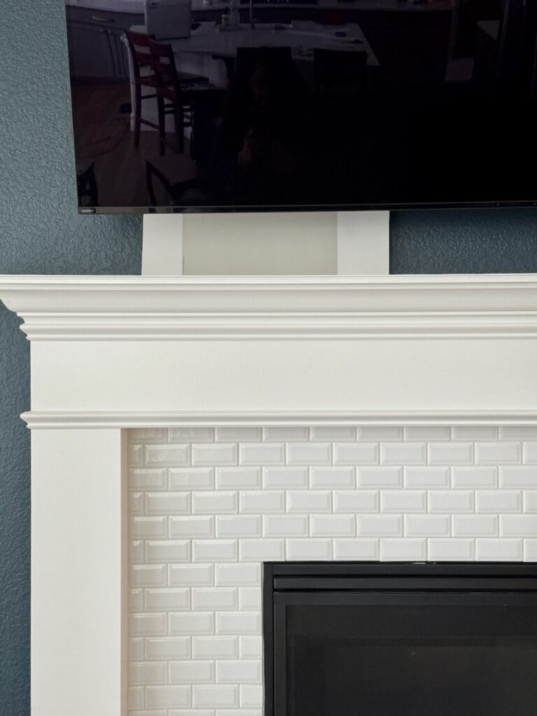 A gray paint color swatch is tested next to a fireplace accent wall.