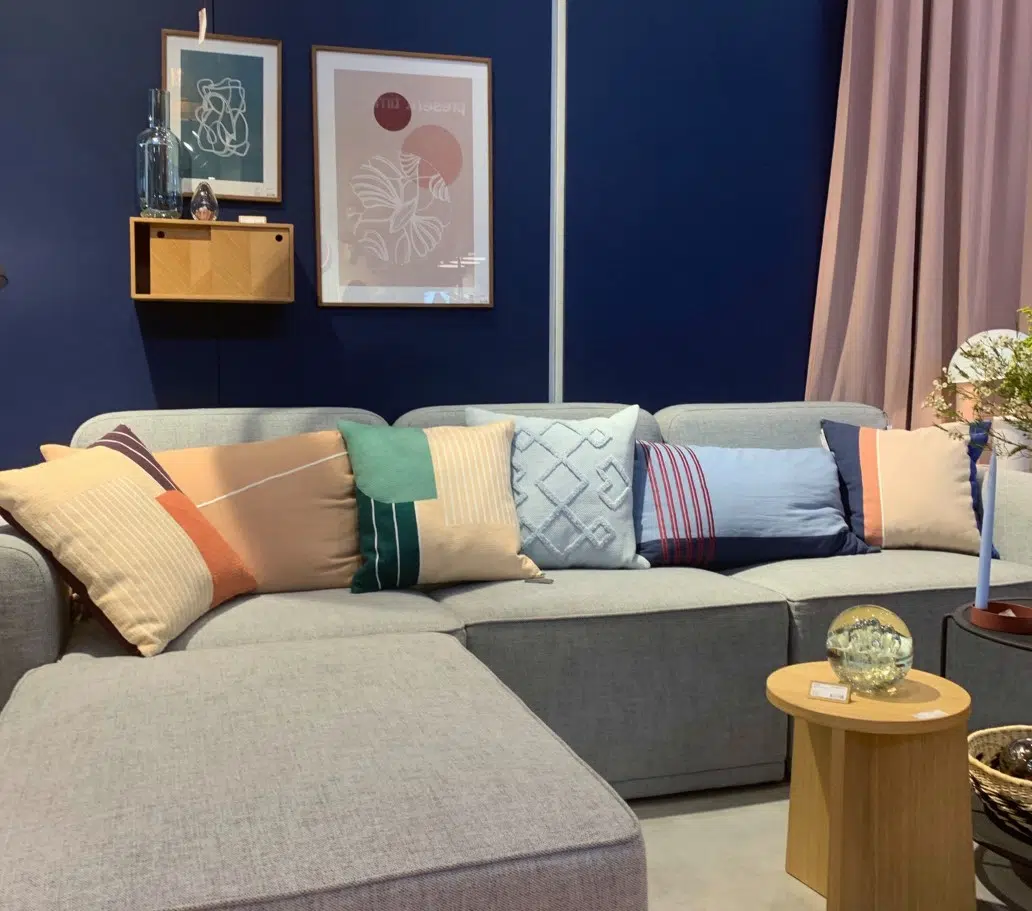 Beige couch with colorful pillows and dark blue walls predict paint color trends