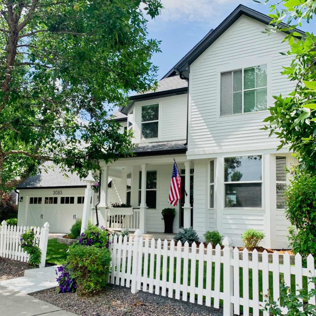 house with farmhouse white paint color, white picket fence and American flag