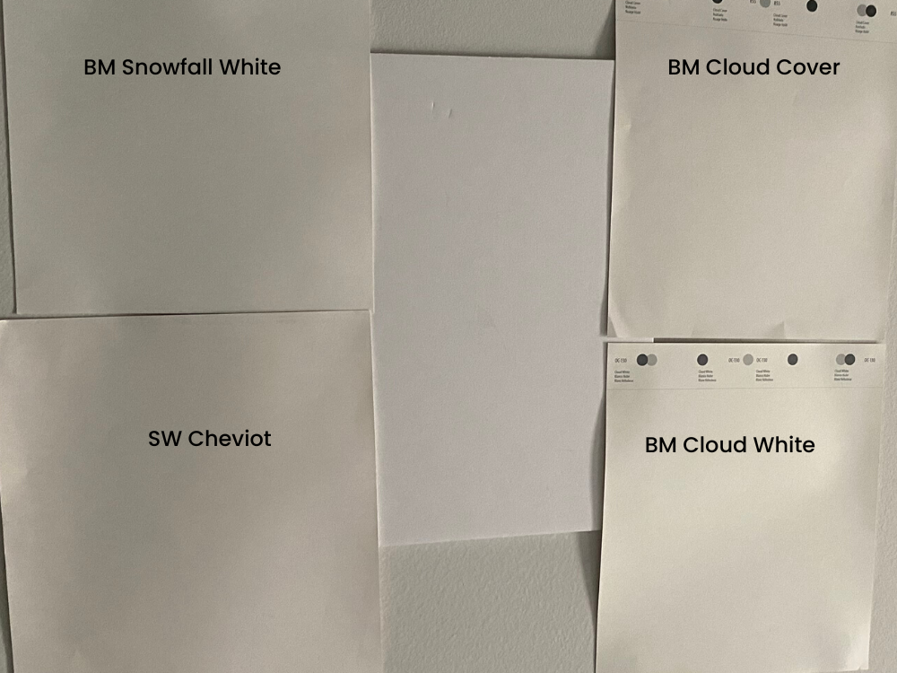 White paint color swatches are tested on a dark basement wall.