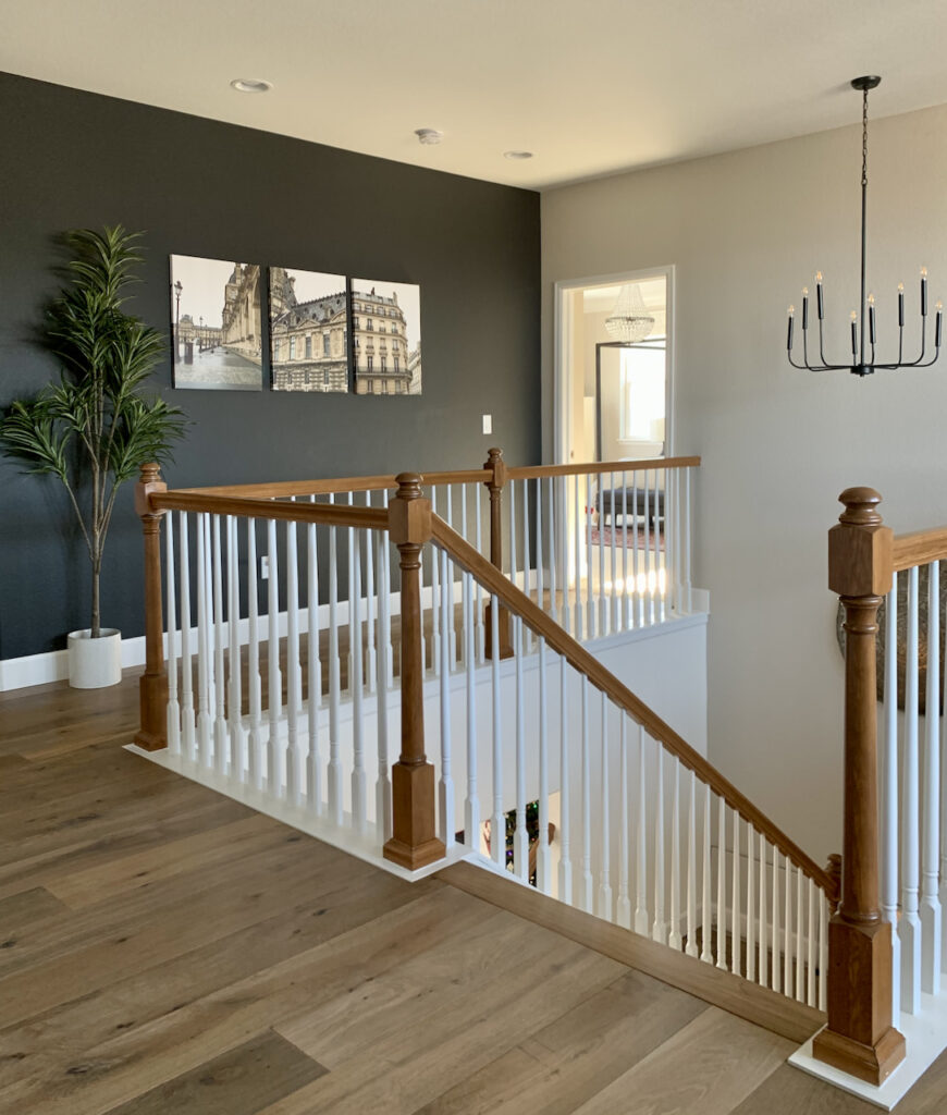 Stairway landing with SW Iron Ore accent wall and SW Agreeable Gray walls with warm hardwood floors.