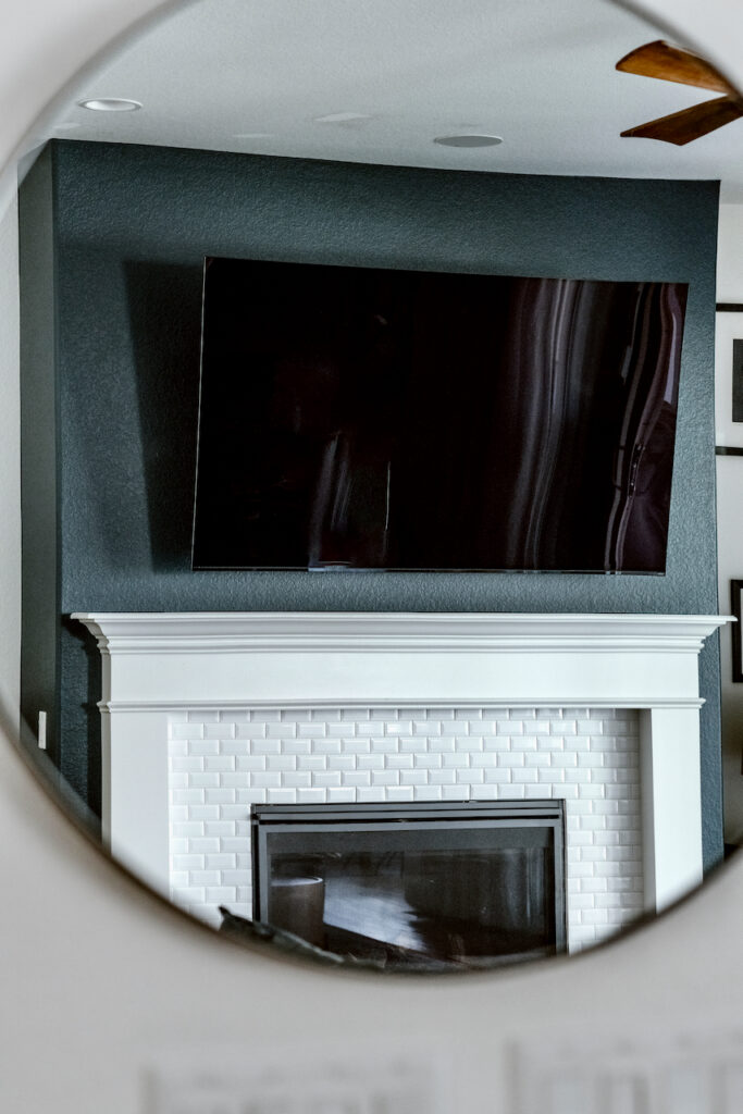 A view in a mirror of a Hague Blue fireplace bump-out with a large TV over the mantle and white brick stone.