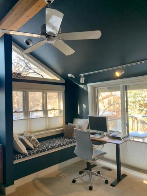 A Farrow & Ball Hague Blue bedroom with an office and seating area in front of large, bright windows.