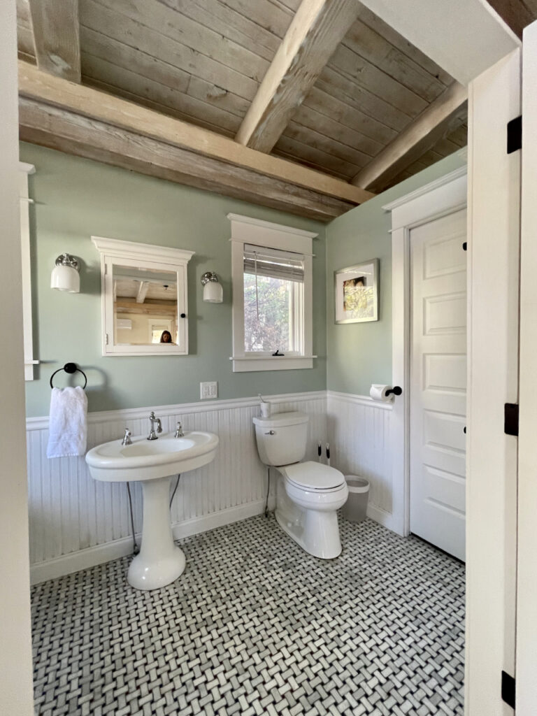 A Farrow & Ball Teresa's Green bathroom with white wainscoting, white sink and wooden ceiling