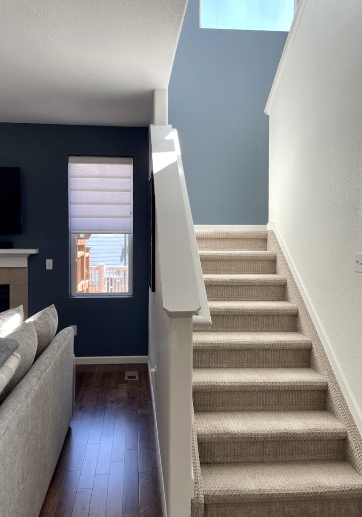 A living room with stairwell with SW Greek Villa paint and Britannia Blue accent walls.