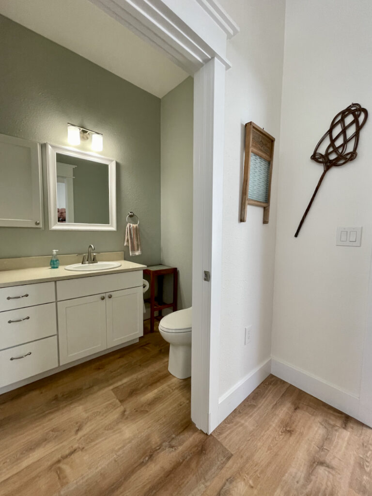 A powder room painted with Benjamin Moore Gray Cashmere paint next to a BM Simply White hallway. 