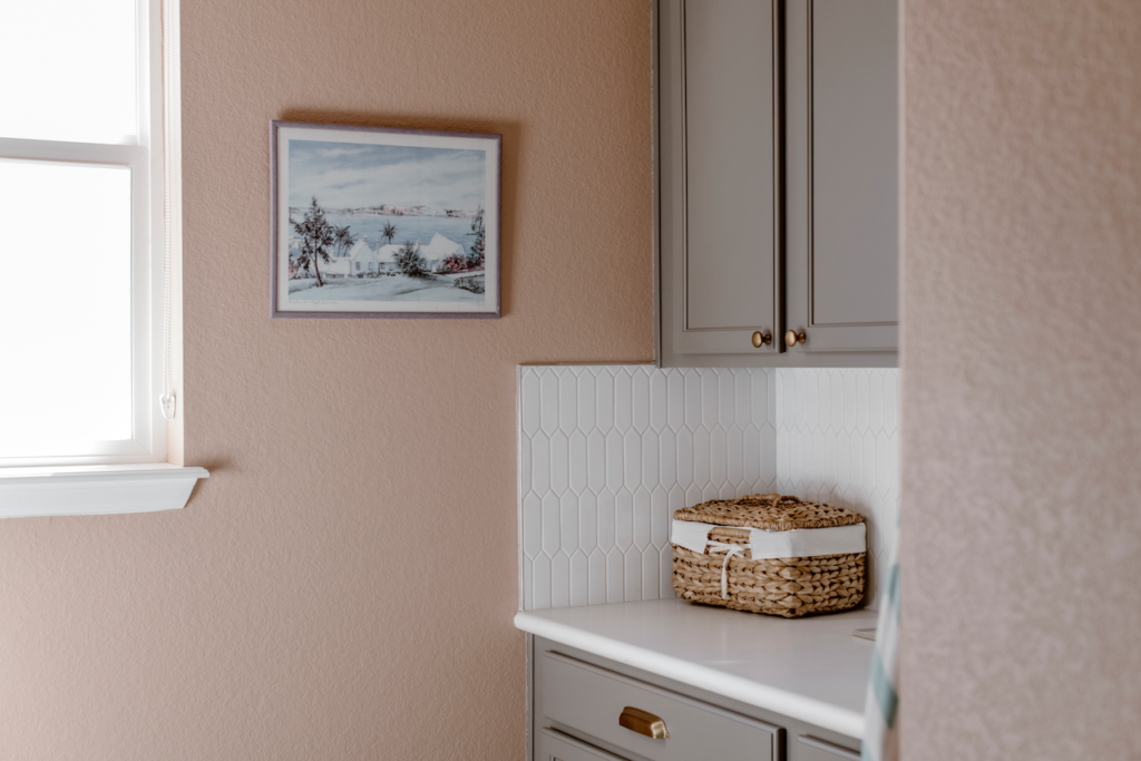 Pink laundry room walls are paired with BM Chelsea Gray cabinets and a white backsplash.