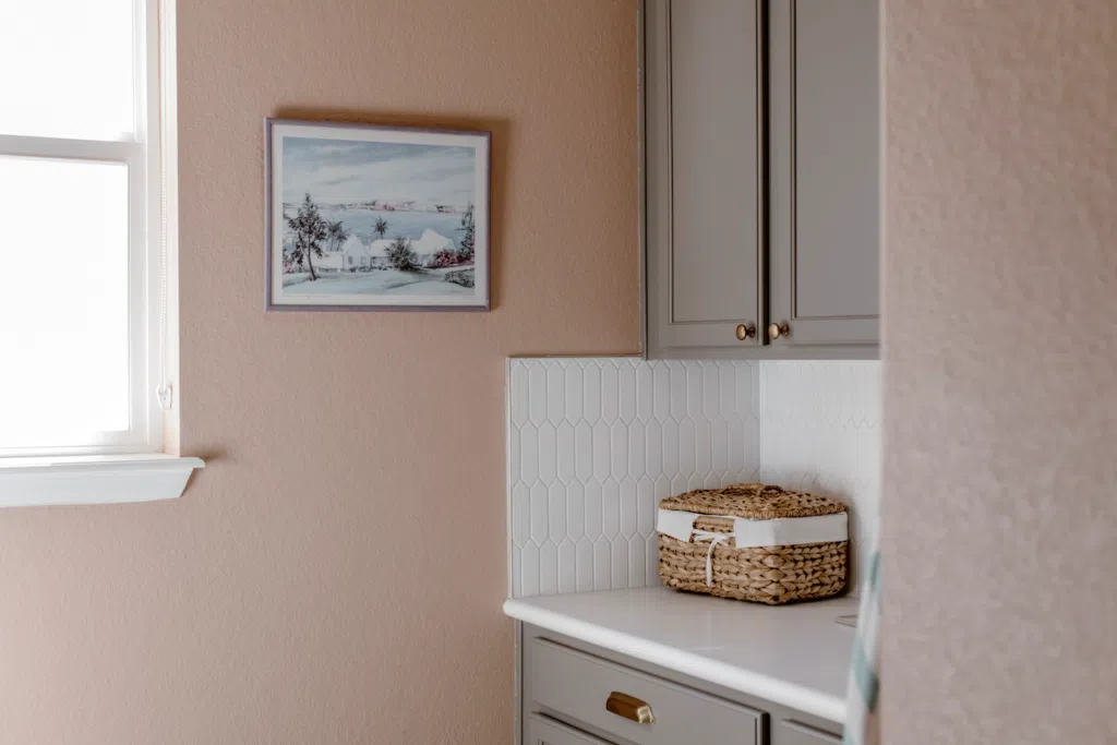 Pink laundry room walls are paired with BM Chelsea Gray cabinets and a white backsplash.