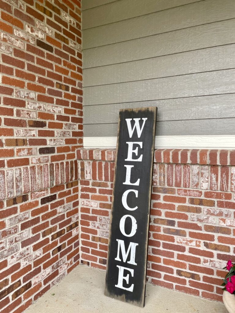 A home with red brick exterior is painted with BM Chelsea Gray paint and features a welcome sign.