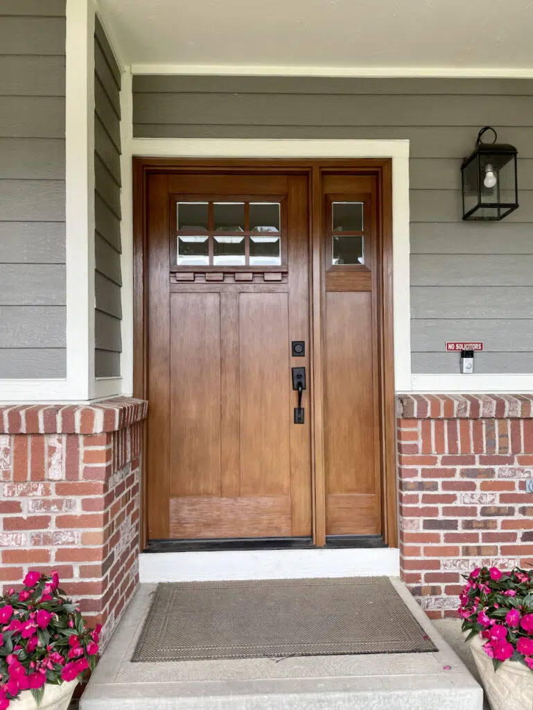 A home is painted with BM Chelsea Gray exterior paint and features red brick accents with a wood front door. 