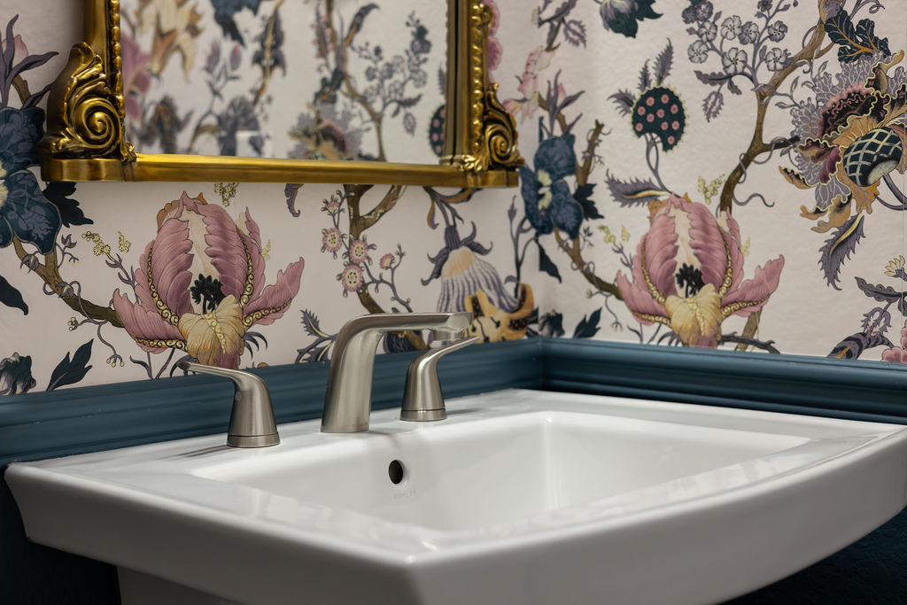 A bathroom sink with floral wallpaper behind it