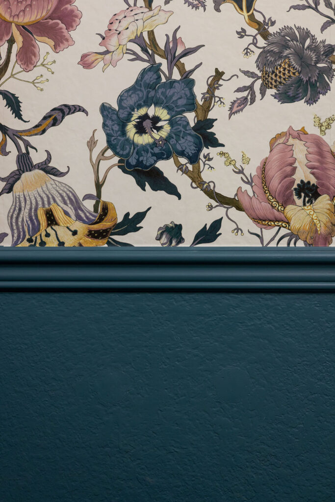 A bathroom wall is painted with BM Bella Blue wainscoting and floral wallpaper.