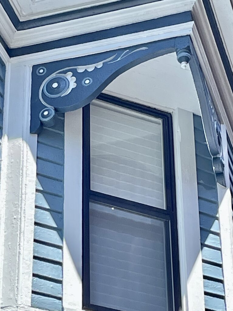 A coastal Victorian home features beautiful exterior window trim and details, including hand-painted floral designs.