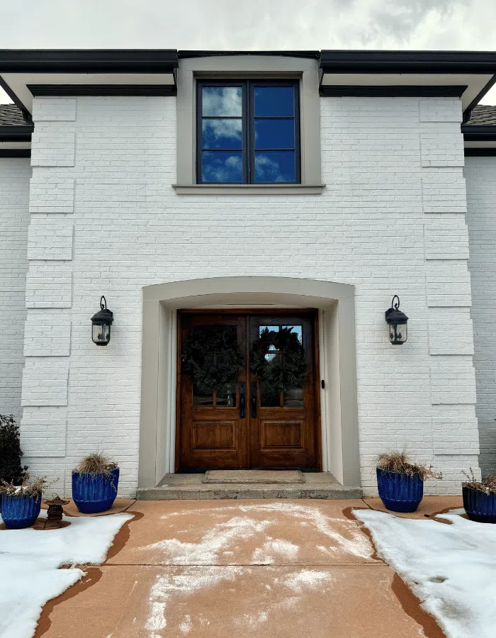 A white painted brick home features soft brown trim and light windows.