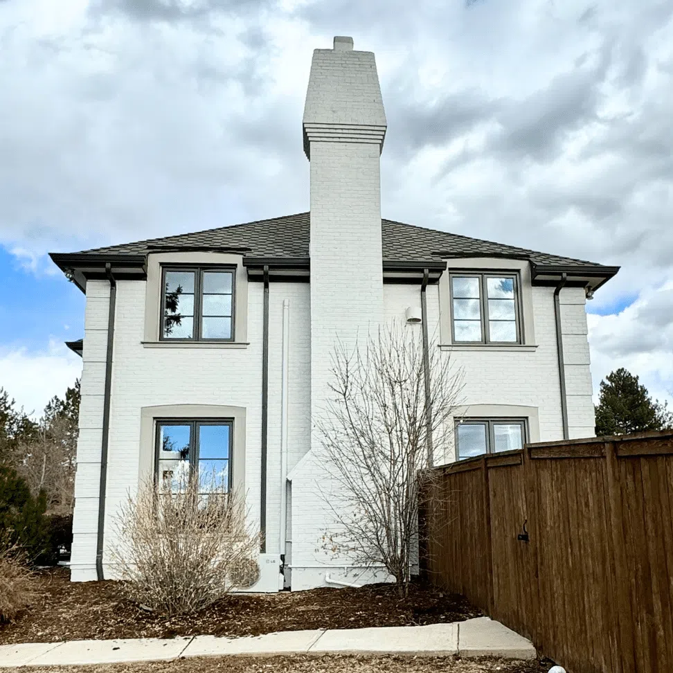 A white painted brick home features soft brown trim and light windows.