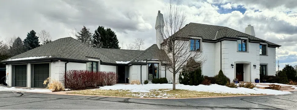 A white painted brick home features soft brown trim and light windows.