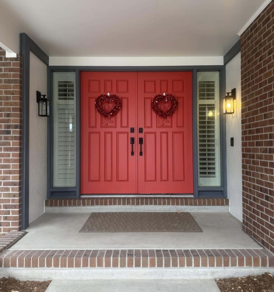 A red brick Tudor home features a SW Habanero Chile front door with SW Web Gray trim and SW Oyster White porch ceiling.