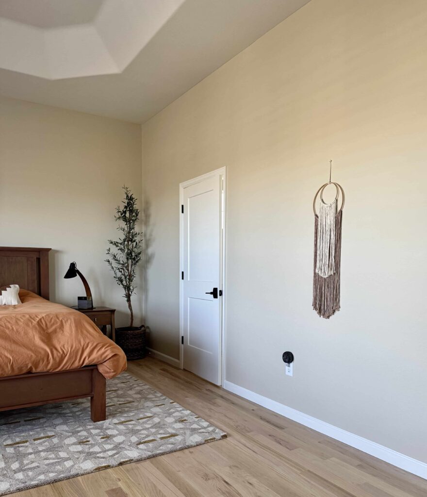 A bedroom features Benjamin Moore Natural Linen wall paint paired with natural greenery.