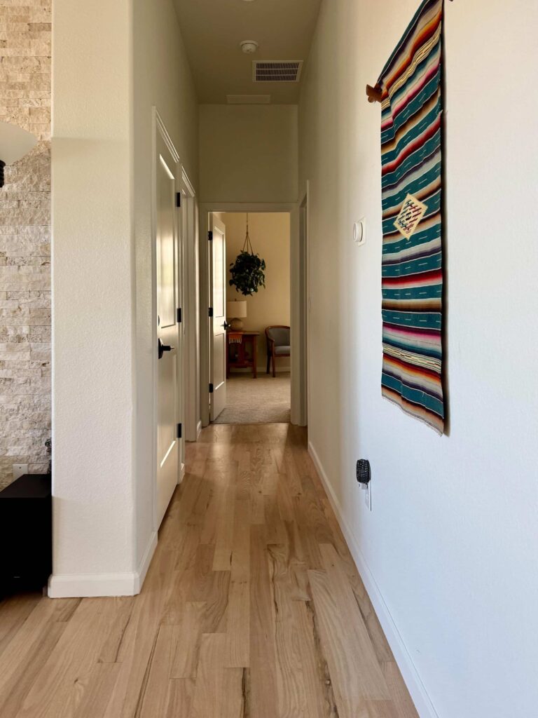 A guest bedroom painted with BM Maritime White paint is visible at the end of a SW Alabaster hallway.