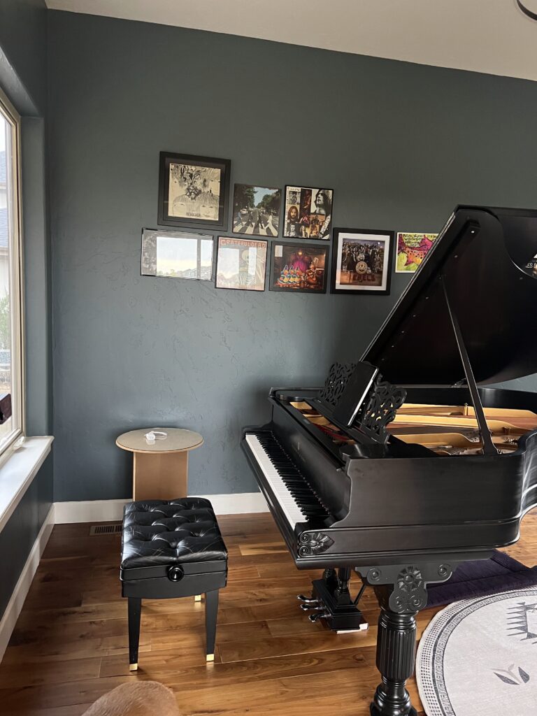 BM Blue Spruce walls alongside a dark wood grand piano with colorful wall decor. 