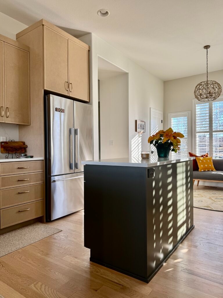 A kitchen features light wood cabinets and SW Alabaster kitchen walls - and a Tate Olive island.