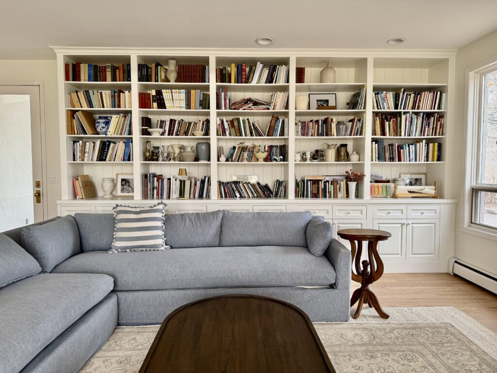 A living room features SW Creamy walls, white built-ins and a blue-gray couch.