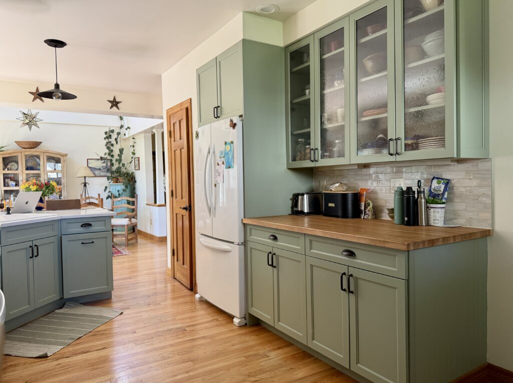 A kitchen features SW Coastal Plains green kitchen cabinets with BM Mascarpone walls.