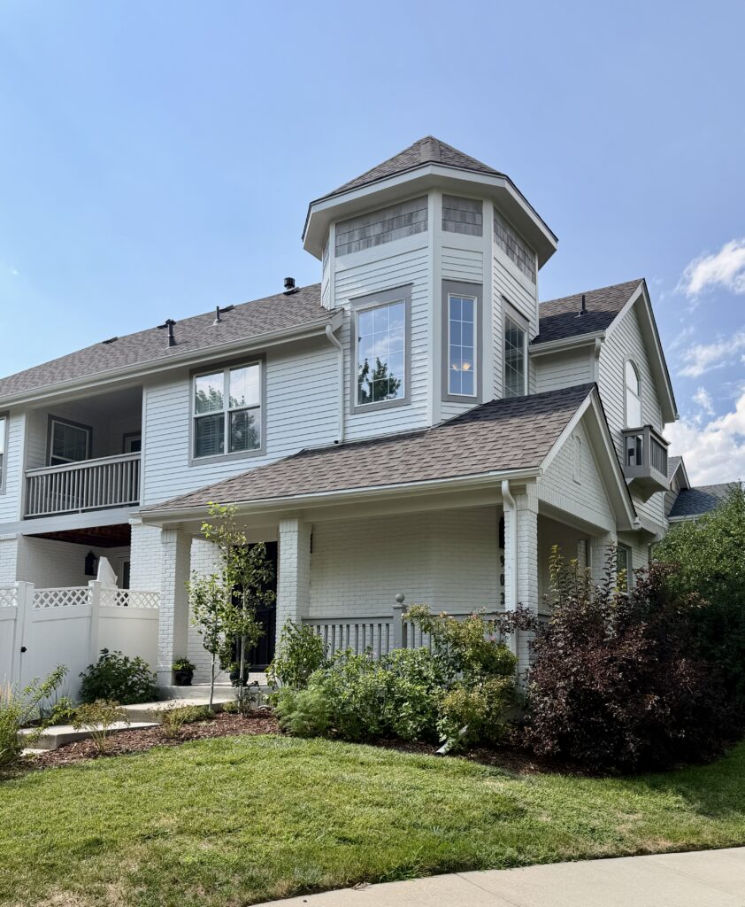 A home painted with Sherwin-Williams White Duck exterior paint features light wood shingles on a unique turret design.