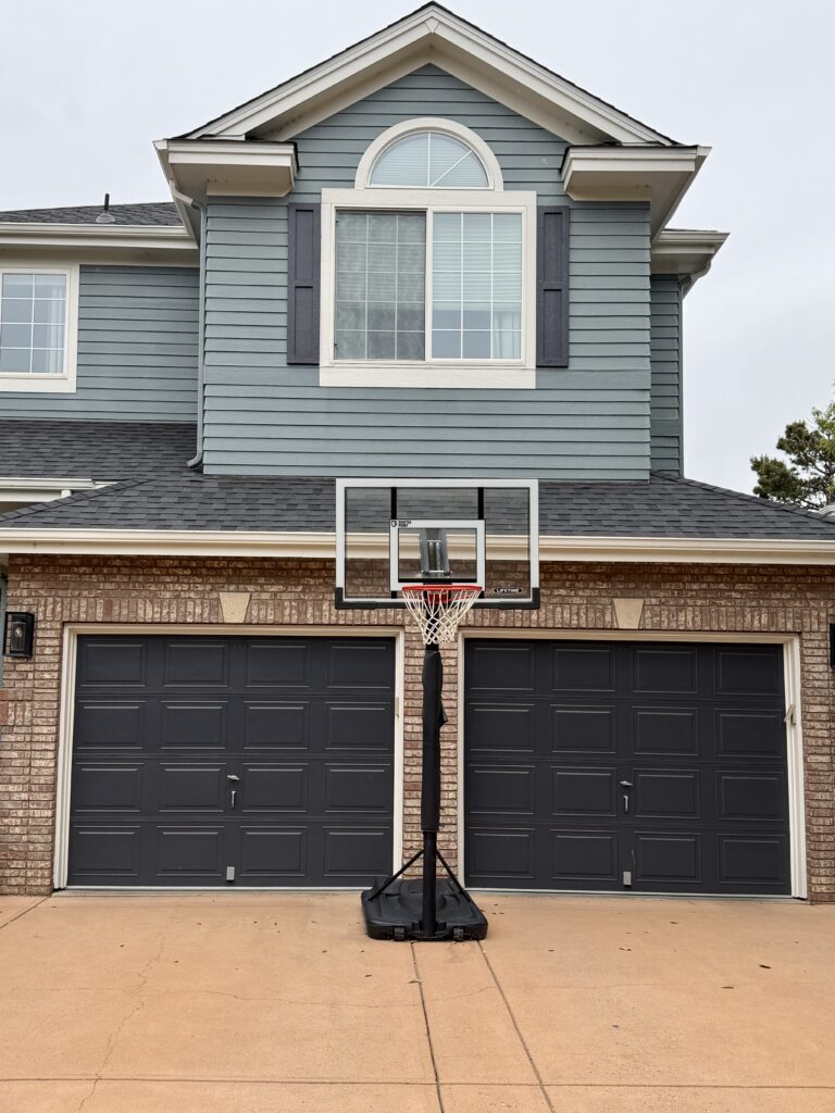 A home features Sherwin-Williams Cyberspace garage doors, alongside red brick finishes and Benjamin Moore Apollo Blue siding.